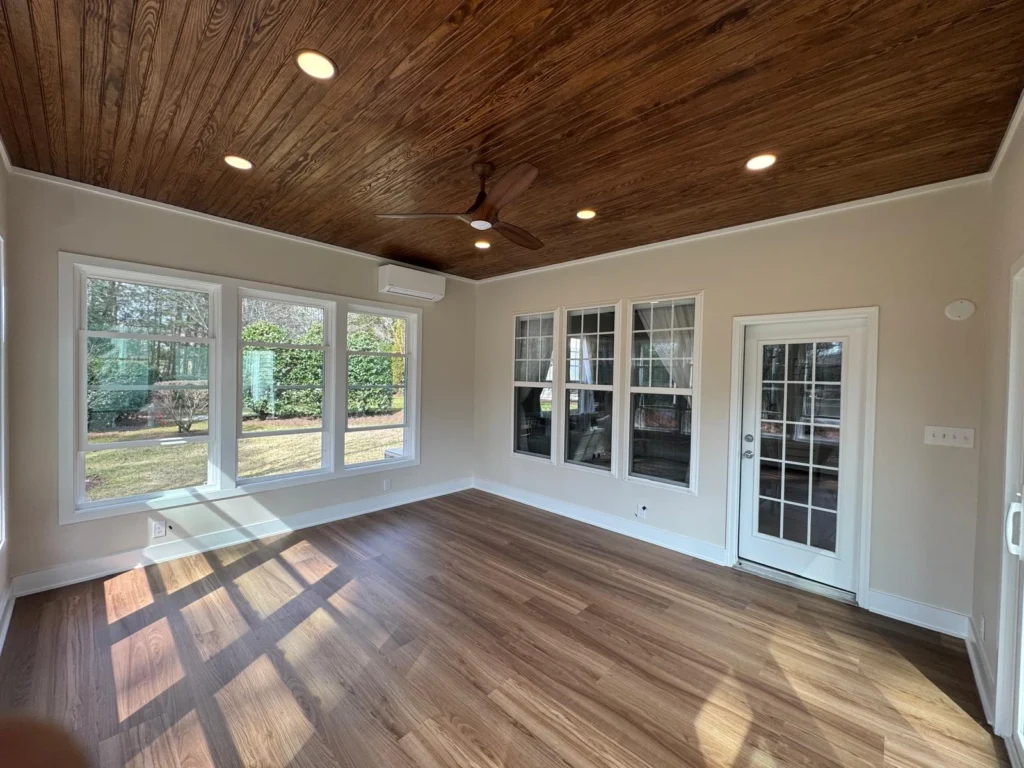 Interior of a finished four-season sunroom in Cary, NC with a wood plank
ceiling, mini-split heating and cooling, and a French door to the main home